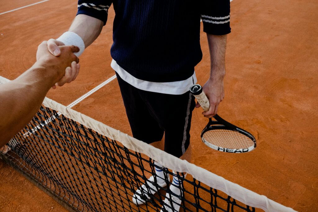 A close-up of tennis players shaking hands over the net on a clay court.